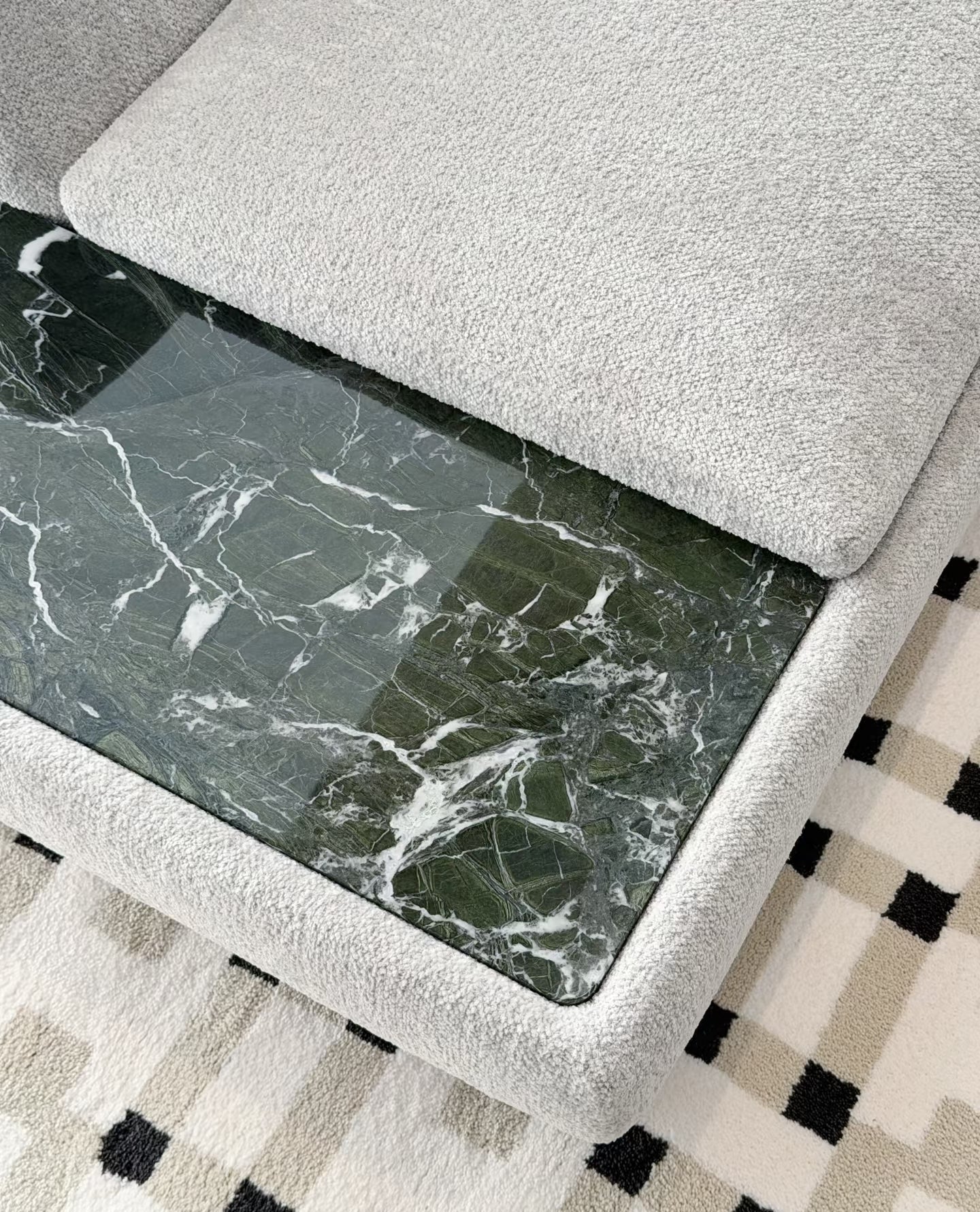 A close-up of the integrated marble side table with a light gray textured fabric cushion and a dark green marble-patterned marble, placed on a black-and-white checkered rug