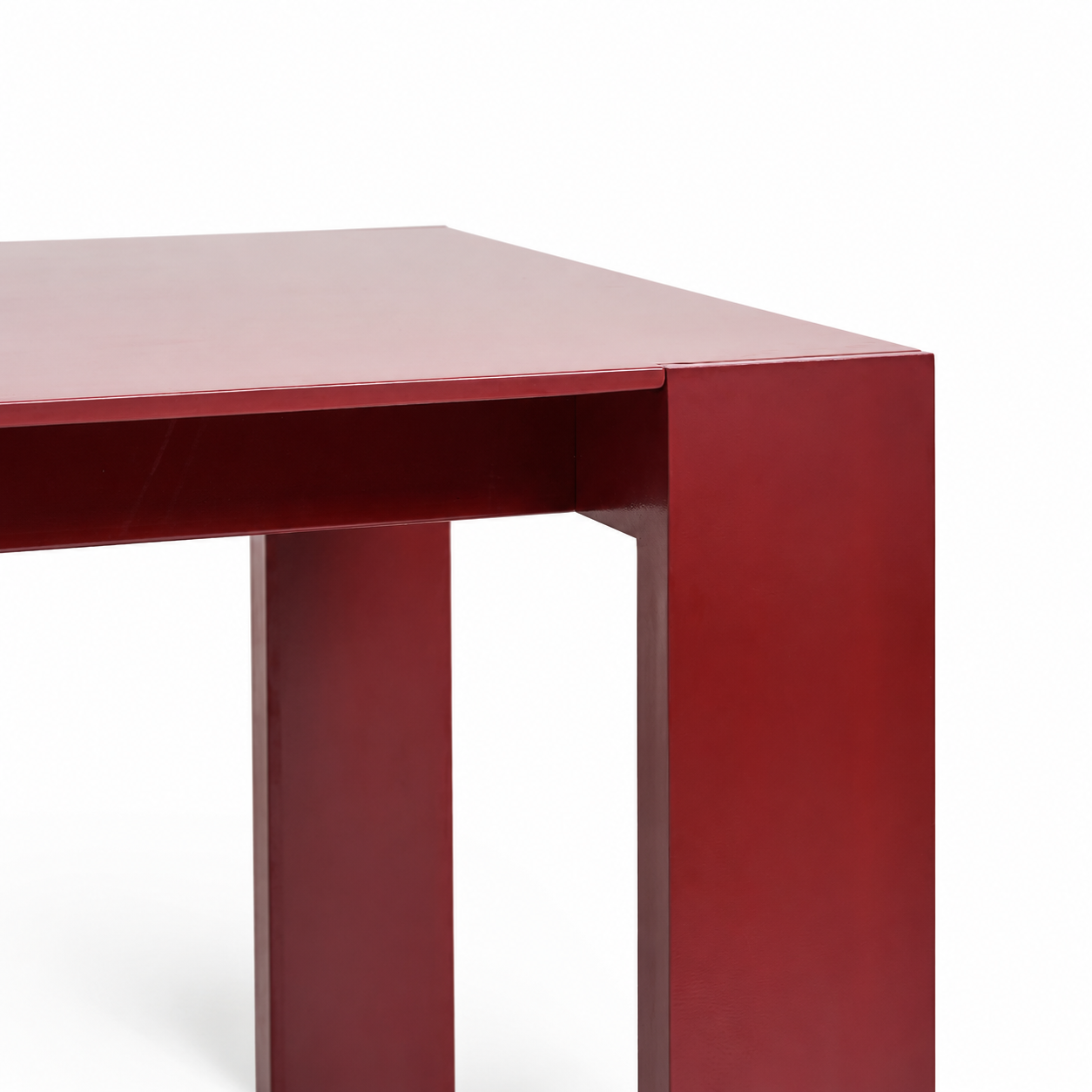 Close-up of a modern rectangular table corner with thick block legs in a glossy deep red finish against a white background.
