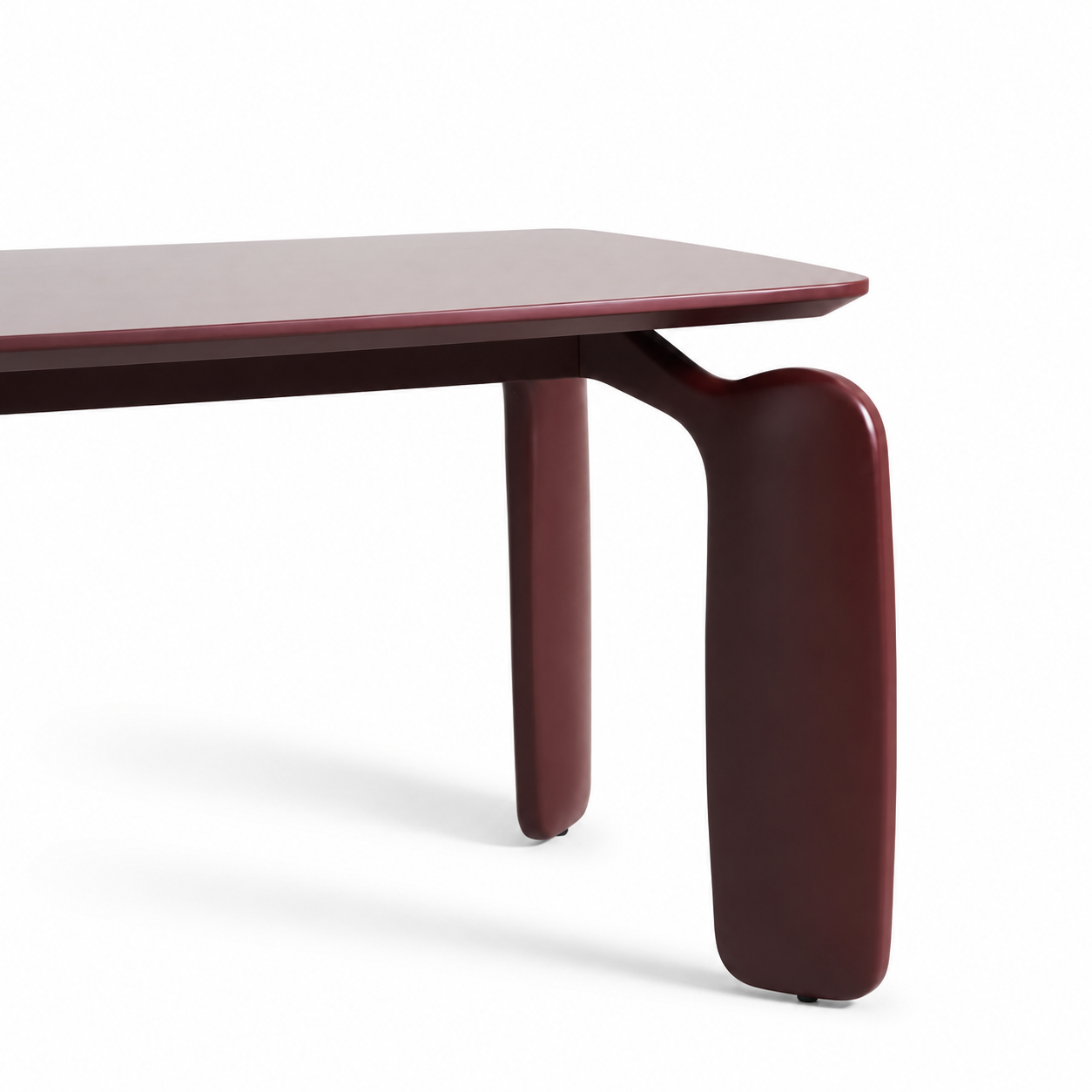 A close-up studio shot of a modern wooden table corner, showing a dark reddish-brown tabletop and matching sculptural leg on a white background.