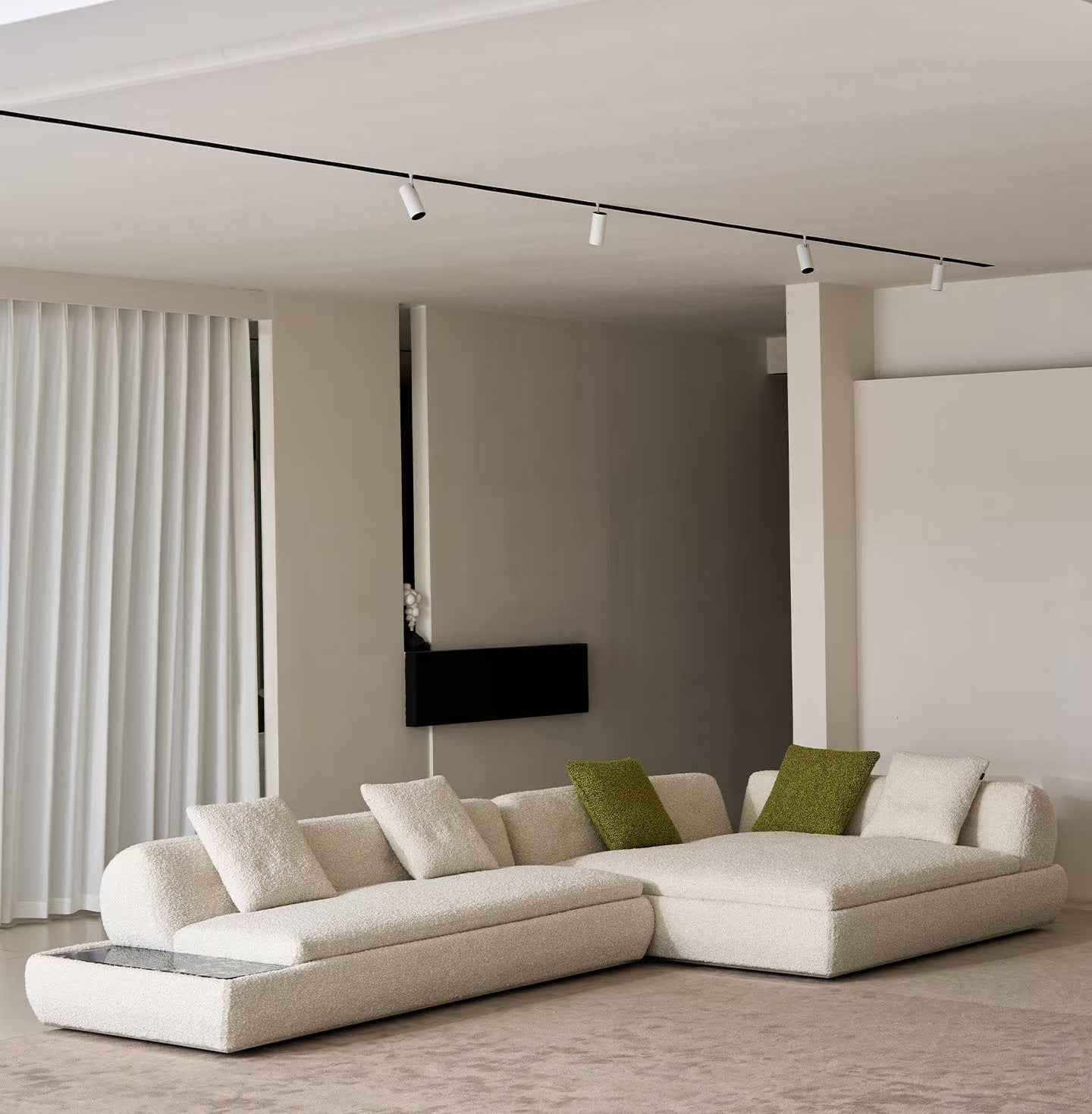 Nocturne sectional sofa in off-white with two green accent pillows, set in a minimalist, contemporary living room with a beige rug and neutral walls.