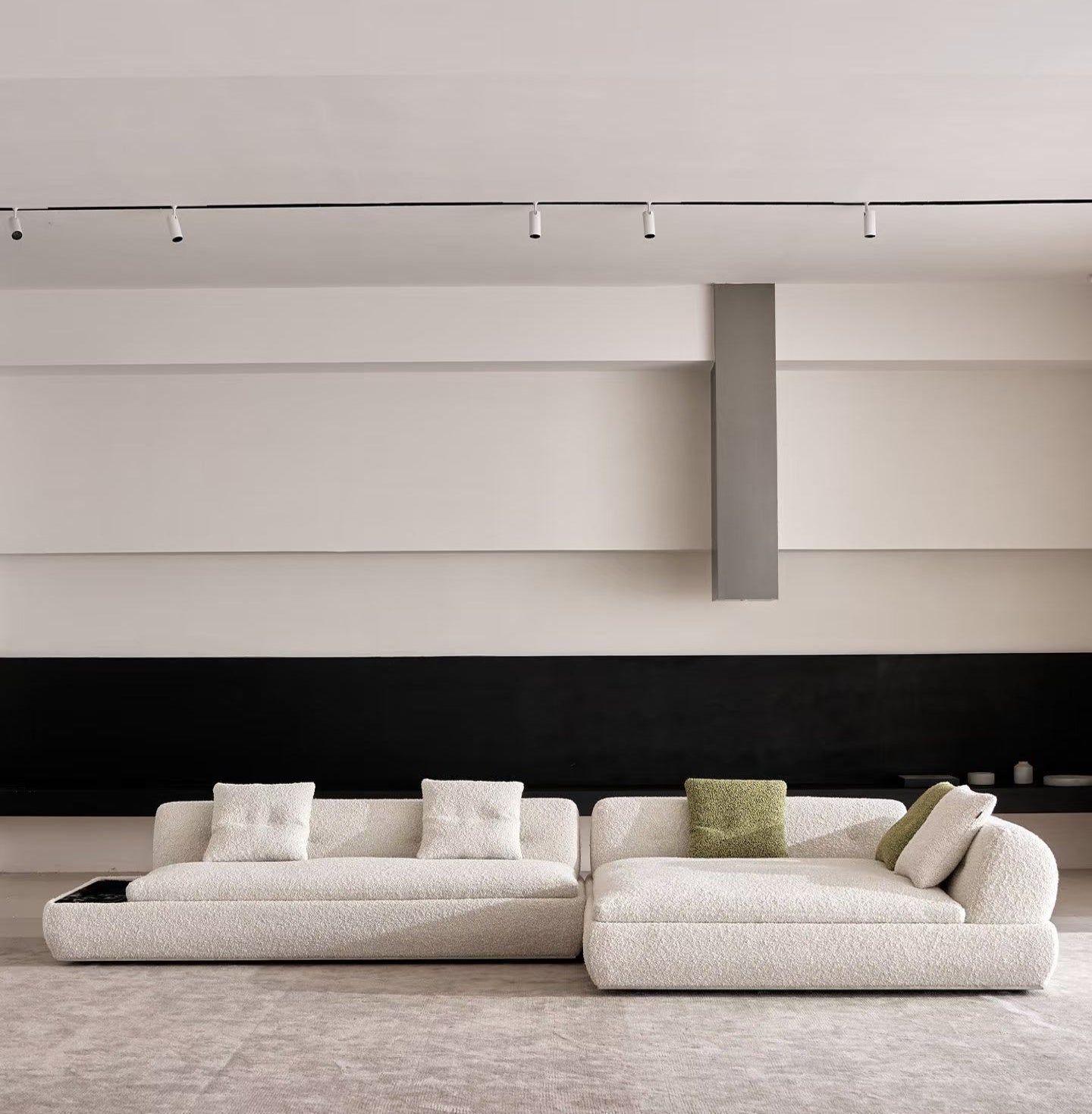 Modern Nocturne low-profile sectional sofa in textured cream bouclé fabric, styled with white and green throw pillows, set against a minimalist wall with a black horizontal band and recessed ceiling track lighting.