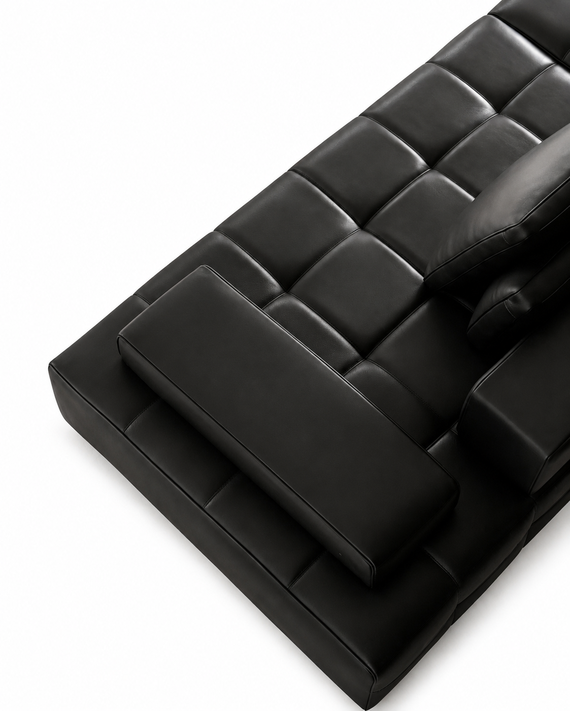 Black tufted leather sofa corner with a matching rectangular accent cushion, photographed on a clean white background.