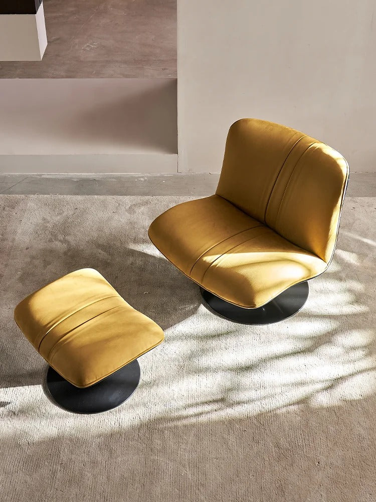 A mustard yellow upholstered swivel chair with a matching ottoman on black circular bases, placed on a textured concrete floor in a minimalist interior setting with natural light shadows.